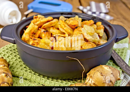 Topinambur arrostito in una teglia, tuberi freschi su un tovagliolo, il misuratore e pillole sullo sfondo delle tavole di legno Foto Stock