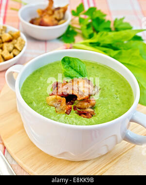 Zuppa verde purea in una ciotola bianca con grigliate di carne e di foglie di spinaci su una tavola di legno sul tessuto di sfondo Foto Stock