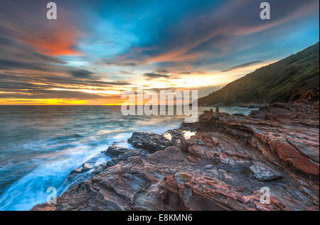 Tramonto onde linea gioco rock di impatto sulla spiaggia e la nebbia Foto Stock