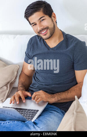 Ritratto di bello sorridente giovane uomo asiatico con la barba utilizzando computer portatile a casa Foto Stock