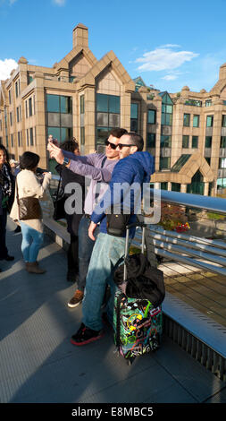 Millennium Bridge, Londra UK. Il 10 ottobre 2014. Due giovani uomini fermano a prendere una foto selfie in autunno sole quanto essi attraversano il millennio o 'traballante ponte' tardi il venerdì pomeriggio. Le previsioni per Londra domani è per una miscela di sparse thundery docce e le magie di sole nel pomeriggio. Credito: Kathy deWitt/Alamy Live News Foto Stock