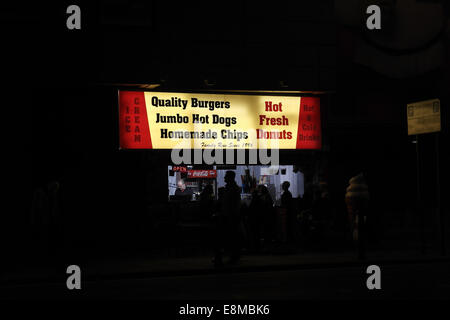 Vista notturna sagome persone che acquistano prodotti alimentari a luci elettriche Jumbo Hot Dogs Burger bar, Central Promenade, Blackpool, Regno Unito Foto Stock