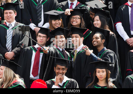 Un gruppo misto di studenti stranieri in abiti tradizionali e di mortaio commissioni tenendo selfie sul giorno di graduazione Aberystwyth University Foto Stock