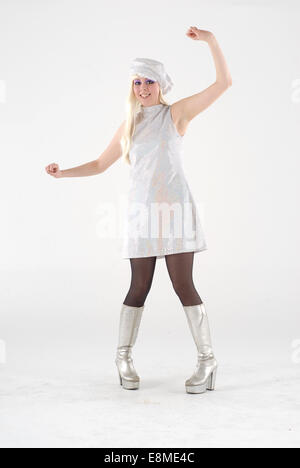 Una ragazza in sessanta fancy dress costume, con stivali di argento e argento gonna e cappello, su sfondo bianco in uno studio fotografico. Foto Stock