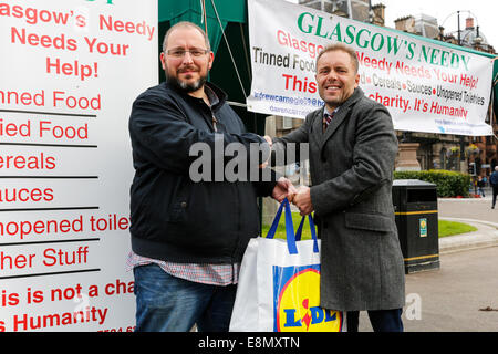 Glasgow, Scozia. Undicesimo oct, 2014. Andrew Carnegie, (destra) 45 invecchiati, da Tollcross a Glasgow, che ha impostato la carità Foodbank 'Glasgow bisognoso" istituito uno stallo in George Square, Glasgow City Centre, al di fuori della City Chambers, con l intenzione di raccogliere contributi e anche il disegno attenzione alle disparità sociali e le necessità dei poveri. Diversi i passanti- da contribuito alla sua carità consegnando in sacchetti di cibo, tra cui Colin Boyd, (sinistra) di 38 anni. Il direttore della società da Kilwinning. Credito: Findlay/Alamy Live News Foto Stock