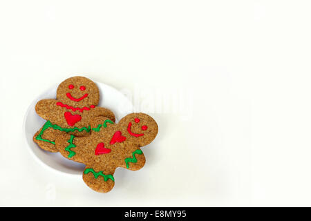 Un Natale di Gingerbread Man cookie con cuori sulla sua maglietta si posa su una piastra bianca con una donna di panpepato, su un bianco isol Foto Stock