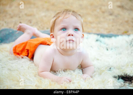 Adorable baby boy cercando mentre appoggiata sulle sue braccia Foto Stock