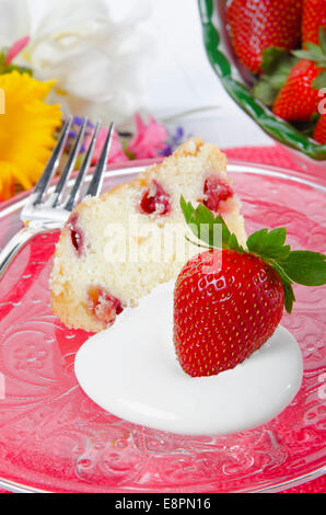 In prossimità di una libbra di fragole la torta con panna montata e illuminazione soffusa. Una tazza di fragole è sfocata in background. Foto Stock