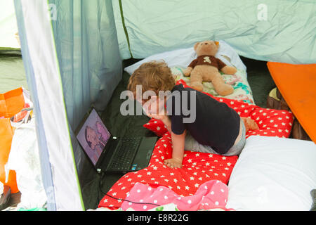 Cinque anni di vecchio ragazzo guardando cartoni animati su un computer portatile mentre il campeggio. Foto Stock