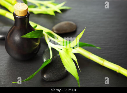 Zen pietre di basalto, bottiglia con un olio per massaggi e bambù su sfondo nero Foto Stock