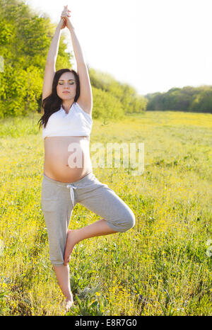 Un sano donna incinta fare yoga nella natura all'aperto Foto Stock