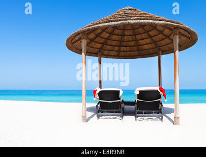 Scheda di Natale o di sfondo - due sedie a sdraio con cappelli di Babbo Natale in piedi sulla splendida spiaggia tropicale con sabbia bianca e turquois Foto Stock