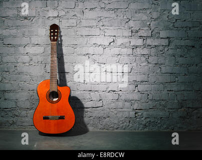 Chitarra acustica appoggiato su una schifezza grigio muro di mattoni Foto Stock