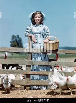Negli anni quaranta anni cinquanta sorridente ragazza TEEN INDOSSANDO PIONEER CALICO vestire il cofano di contenimento cesto uovo guardando la fotocamera Foto Stock