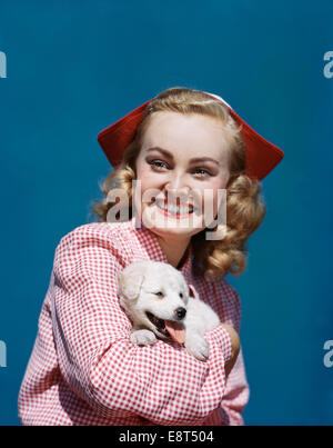 Negli anni quaranta anni cinquanta ritratto bionda sorridente ragazza TEEN indossando il bianco e il rosso controllato camicetta e stile olandese HAT HOLDING SPITZ cucciolo Foto Stock