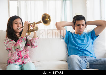 Fratello ispanica che copre le sue orecchie come sorella practice tromba in salotto Foto Stock