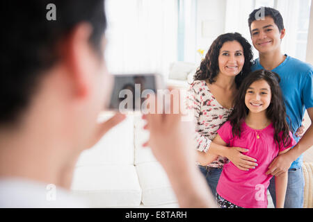 Famiglia di origine ispanica tenendo cellulare fotografia in salotto Foto Stock