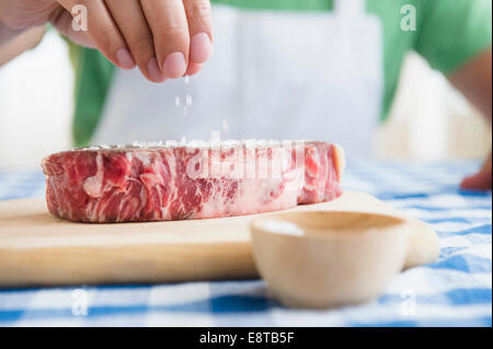 Close up di razza mista uomo spargendo il sale sulla bistecca Foto Stock