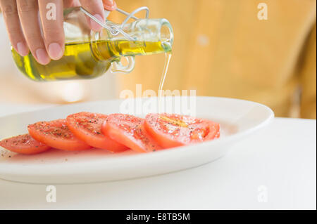 Close up di razza mista uomo versando olio per i pomodori Foto Stock