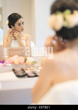 Razza mista, Asian / American sposa in bianco abito da sposa mette il trucco e orecchini prima del matrimonio Foto Stock