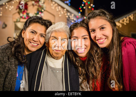 Tre generazioni di donne ispaniche in piedi fuori casa decorata con luci di stringa Foto Stock