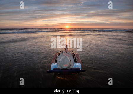 Uomo caucasico in sedia a sdraio affacciato sul tramonto sulla spiaggia Foto Stock