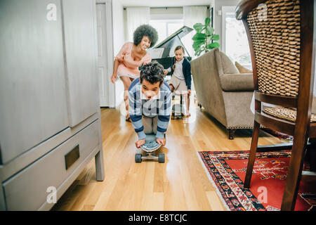 Razza mista famiglia guardare boy ride skateboard in salotto Foto Stock