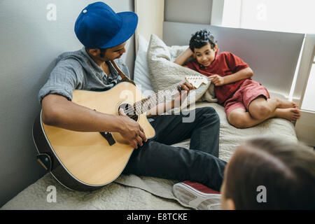Razza mista boy guardando il fratello a suonare la chitarra in camera da letto Foto Stock