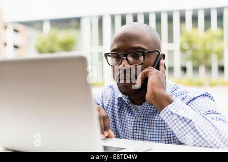 Uomo nero mediante telefono cellulare e computer portatile all'aperto Foto Stock