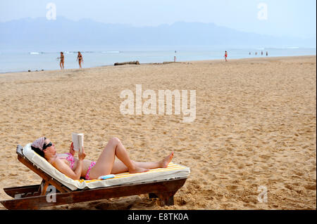 La donna a prendere il sole sulla spiaggia con libro Foto Stock