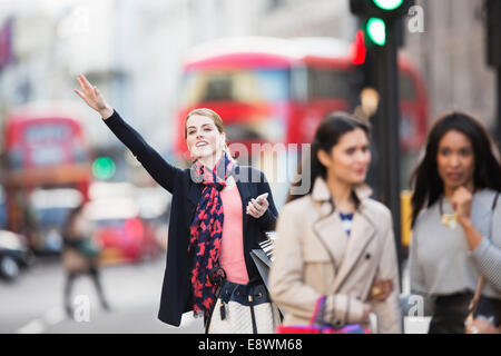 Segnalazione di donna per taxi sulla strada di città Foto Stock