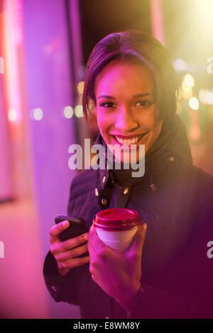 Donna su una strada di città con caffè e telefono cellulare di notte Foto Stock