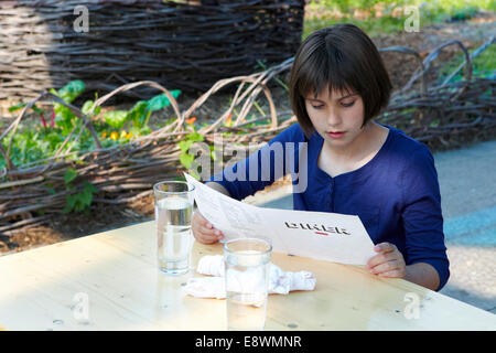 11 anno vecchia ragazza guardando il menu del ristorante Foto Stock