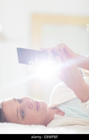 Donna che utilizza il telefono cellulare sul letto Foto Stock