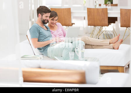 Paio utilizzando laptop insieme sul divano letto nel soggiorno moderno Foto Stock