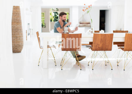 Uomo con tavoletta digitale al tavolo per la colazione nella sala da pranzo moderna Foto Stock