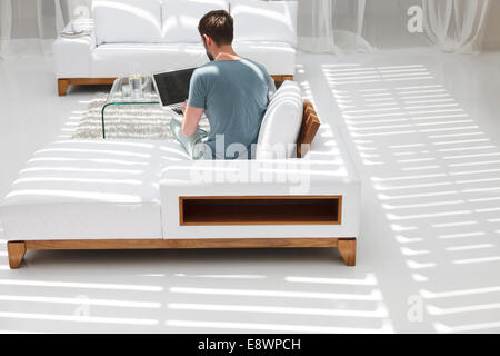 Uomo che utilizza sul computer portatile sul divano nel soggiorno moderno Foto Stock