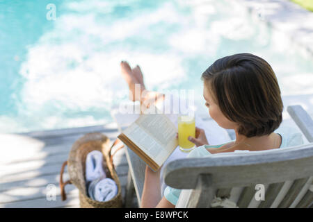 Elevato angolo di visione della donna di lettura e di bere succo di frutta da piscina Foto Stock