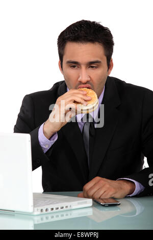 Imprenditore di mangiare un hamburger alla sua scrivania Foto Stock