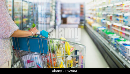 Donna piena di spinta carrello acquisti nel negozio di alimentari Foto Stock