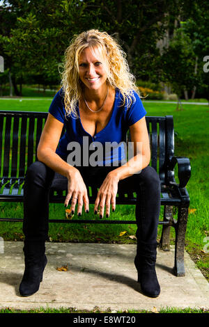 Modello femminile in abbigliamento casual seduto su una panchina nel parco Foto Stock