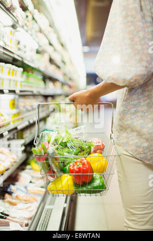 La donna che porta la piena Shopping basket in negozio di alimentari Foto Stock