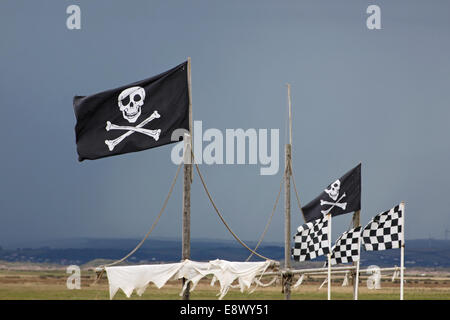 Bianco e nero bandiere pirata battenti alto da un gioco di nave a montanti in una giornata di vento nel Devon, Regno Unito Foto Stock