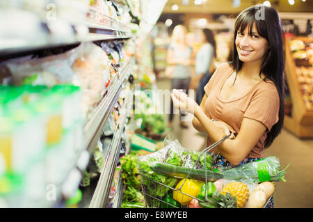 La donna che porta la piena Shopping basket in negozio di alimentari Foto Stock