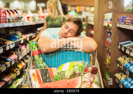 Uomo dorme sul carrello spesa nel negozio di alimentari Foto Stock