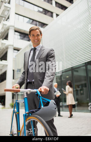 Imprenditore bicicletta a piedi al di fuori dell'edificio degli uffici Foto Stock