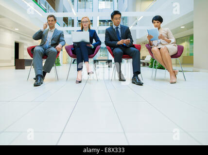 La gente di affari sat in sedie lavorando in ufficio edificio Foto Stock