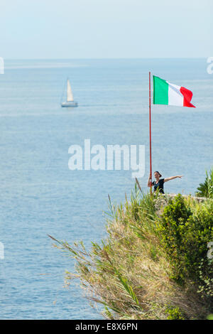 Donna attraente in piedi dalla bandiera italiana, il mare con barche in background Foto Stock