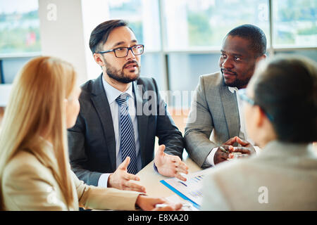 Imprenditore gravi di etnia asiatica parlare mentre i suoi colleghi ascoltando lui alla riunione Foto Stock
