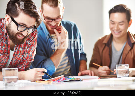 Tre progettisti allegro scegliendo colori da tavolozza Foto Stock